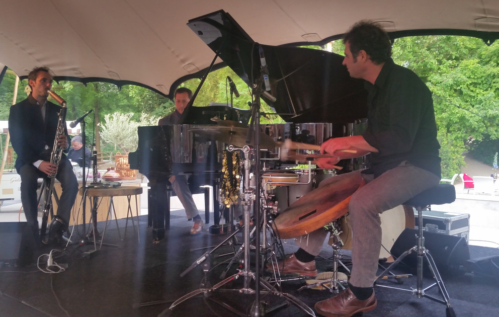 Trio met saxofoon, piano en drums onder een overkapping